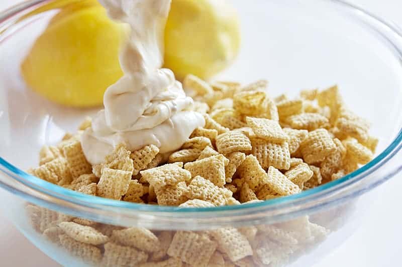 Lemon Puppy Chow (aka Muddie Buddies) is a super fun citrus twist on a classic! Sweet vanilla and lemon flavor all wrapped up in an easy-to-eat snack! #lemonpuppychow #lemonmuddiebuddies #puppychow #puppychowrecipe #muddiebuddies #easysnacks #snacks #afterschool #iambaker #nobake 把巧克力倒在麦片上给小狗吃