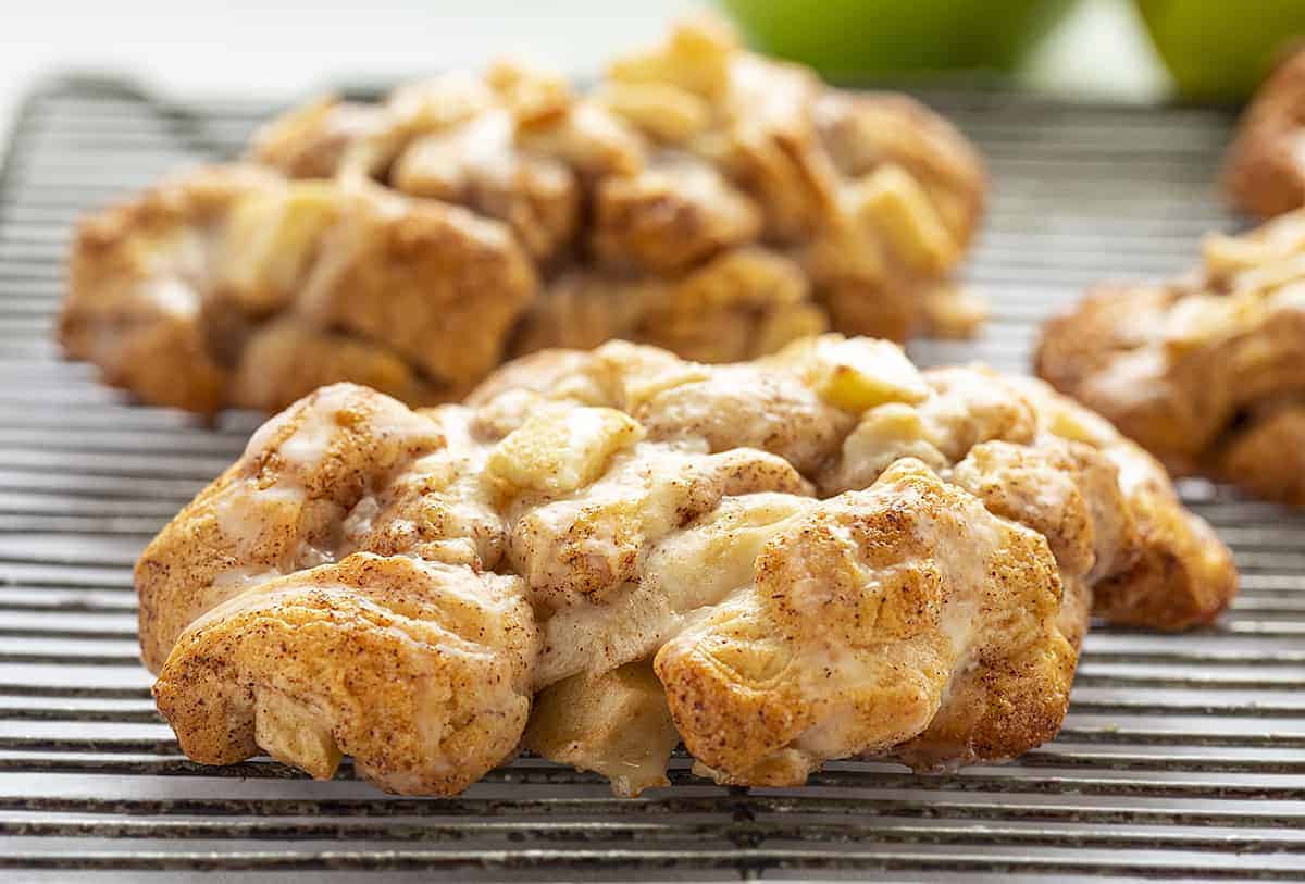 Baked Apple Fritters are a quick and easy way to enjoy an Apple Fritter without any deep-frying or oil! Baking Apple Fritters, Baked Fritters, Apple Fritters, Fritters with Real Apples, Baking, Recipes, Dessert, Breakfast, i am baker, iambaker 在冷却架上冷却的烤苹果馅饼,后面放青苹果