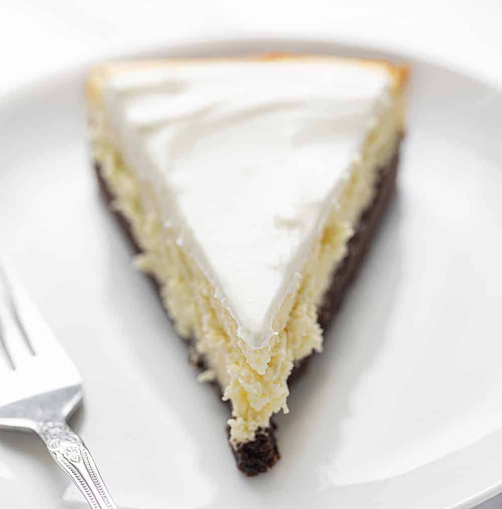 一块布朗尼底芝士蛋糕放在白色盘子里，旁边放着叉子