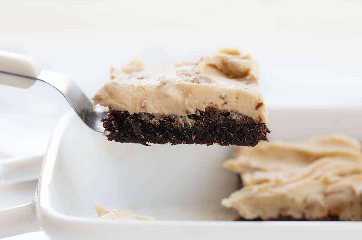 Butterfinger Brownies are fudgy and perfectly baked brownies topped with a sweet homemade Butterfinger frosting! Butterfinger Brownies, Butterfinger Brownie Recipe, Butterfinger Frosting, Butterfinger Buttercream, baking, recipes, iambaker, i am baker, dessert 铲子拿着一块奶油巧克力蛋糕