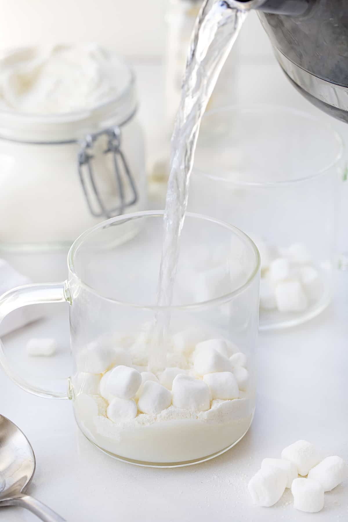 把热水倒在白巧克力，热可可混合物和迷你棉花糖在一个透明的杯子。
