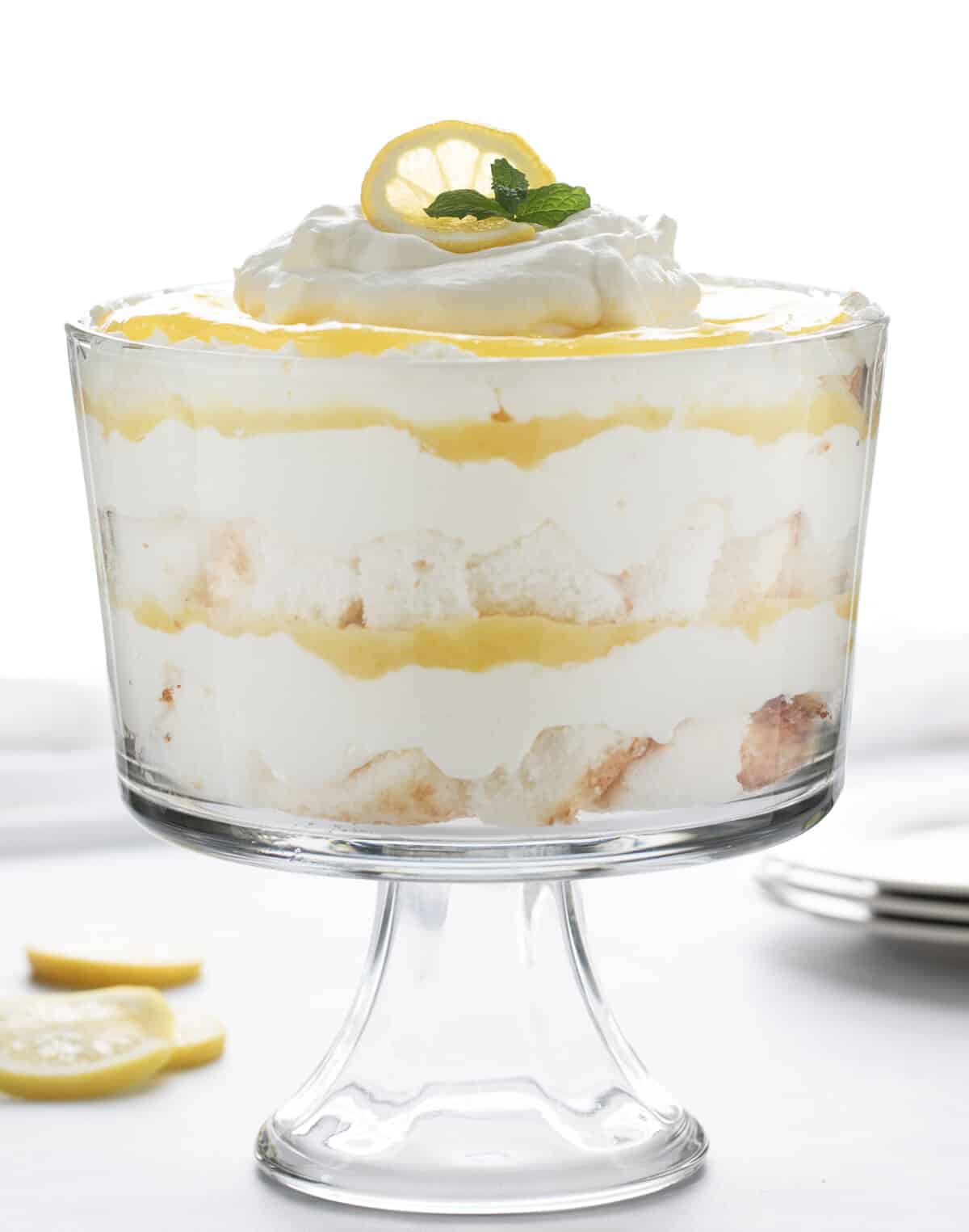 柠檬奶油蛋糕在白色柜台玻璃蛋糕盘与柠檬和盘子。