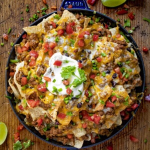 用的锅牛肉烤干酪辣味玉米片,上面有融化的奶酪,番茄,酸奶油和石灰。