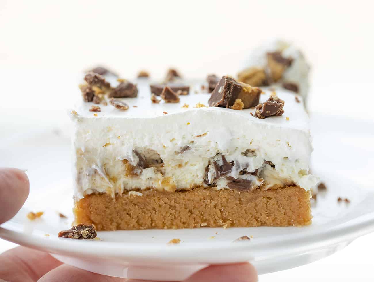 Hand Holding Up a Plate with Reese Peanut Bar on It and Sprinkled with Chopped Reeses