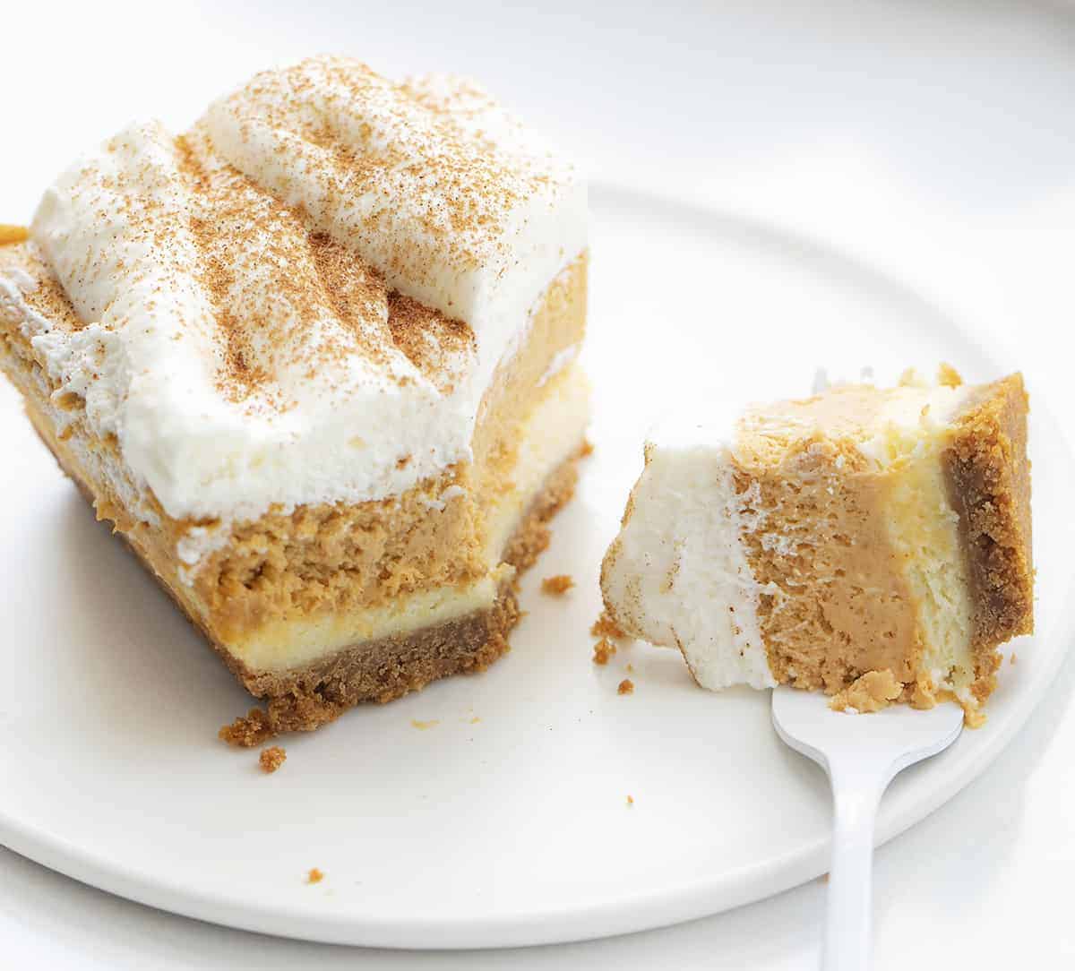 一块南瓜芝士蛋糕，用叉子咬。南瓜甜点，甜点，烘焙，秋天烘焙，甜点食谱，南瓜芝士蛋糕，全麦饼干皮，奶油浇头，足球甜点，超级碗甜点，圣诞甜点，我是面包师，iambaker