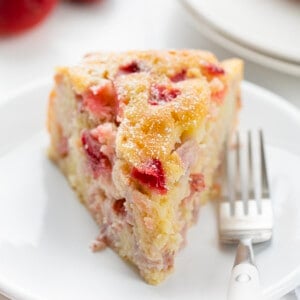 一块新鲜草莓蛋糕放在白色盘子上，草莓为背景。